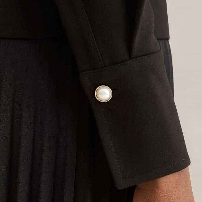 A single faux-pearl button signs off the collar and mirrors the same ones stitched at the cuffs.  