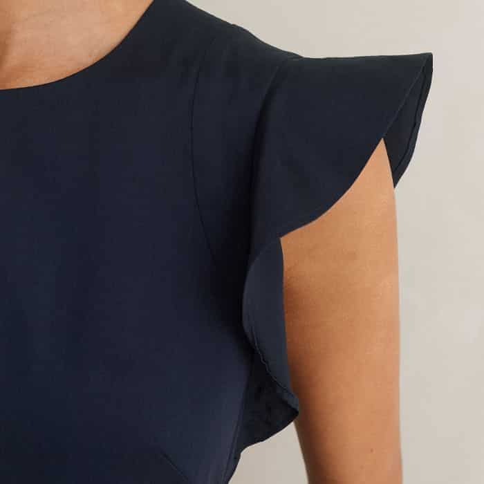 The armholes are decorated with a ruffled trim for a flattering finish.