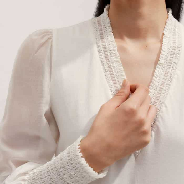 The V-neckline is lined with a ruffled trim that can be left on display when the piece is worn under complementary knits.