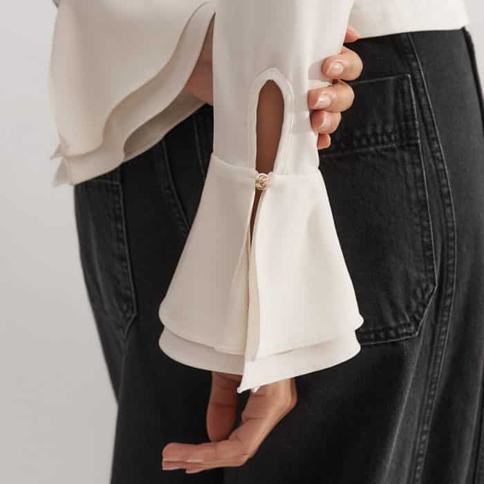 The full-length sleeves fall to feminine flared sateen cuffs with gold-toned buttons.