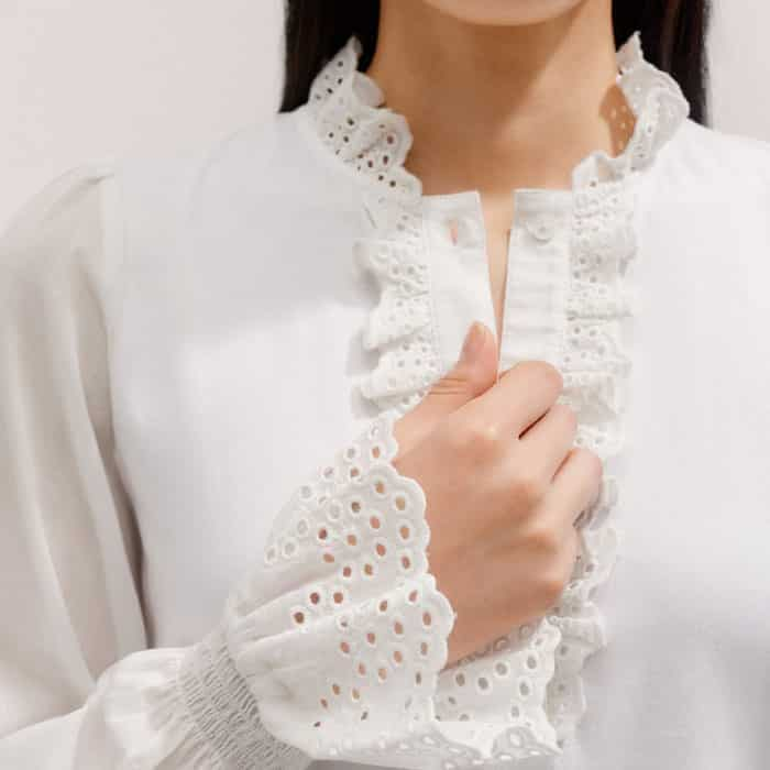 The placket and sleeves are elevated with a ruffled, broderie trim for a feminine finish.