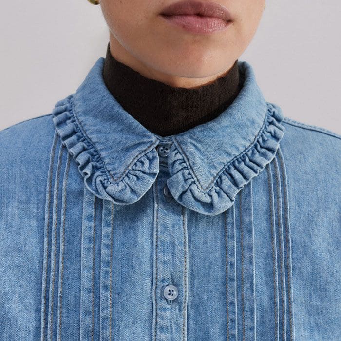 The collar is trimmed with a ruffled edge for a feminine finish.